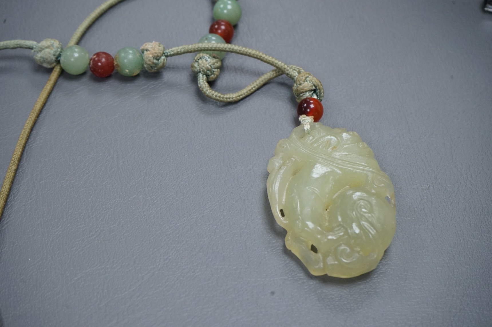 A Chinese carved bowenite jade pendant, on knotted beaded cord, pendant 6cm long.